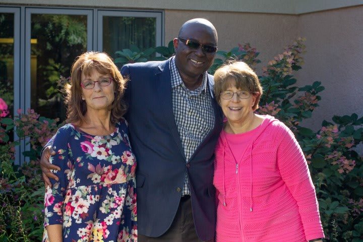 Three people standing together outside, smiling at the camera.
