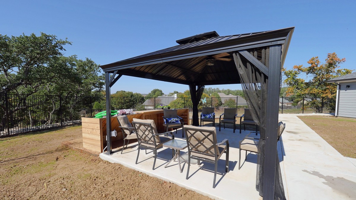 A cozy outdoor seating area under a gazebo in a sunny backyard.