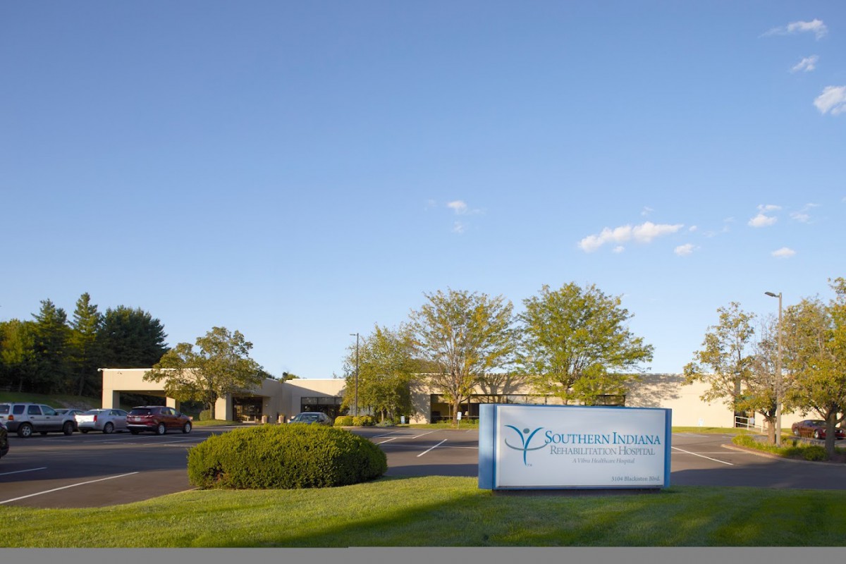 A view of a building with a sign in front, surrounded by trees and grass under a clear sky.