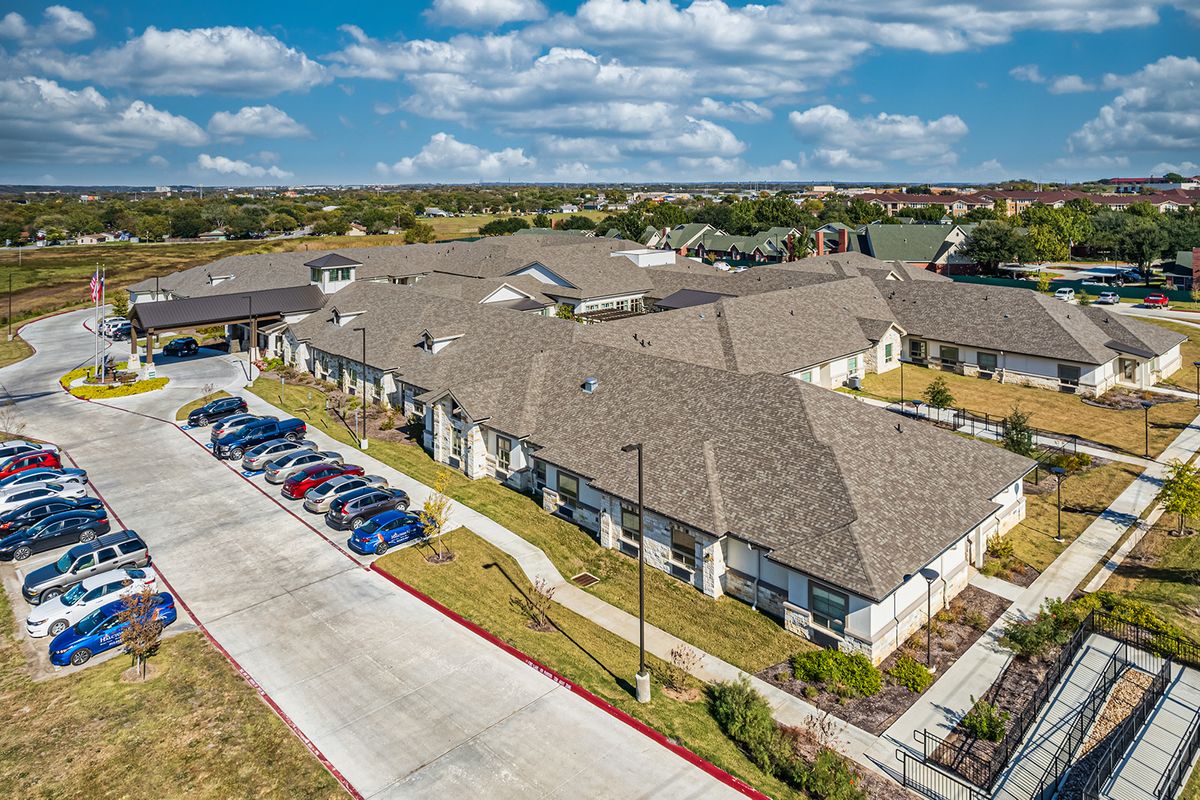 Aerial view of a residential building with a parking lot under a cloudy sky.