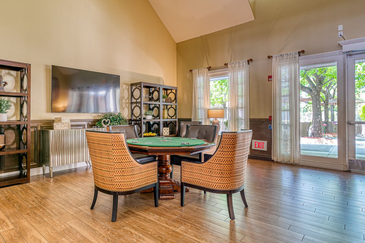 A cozy living room with a dining area featuring wicker chairs, wood flooring, and a television mounted on the wall.