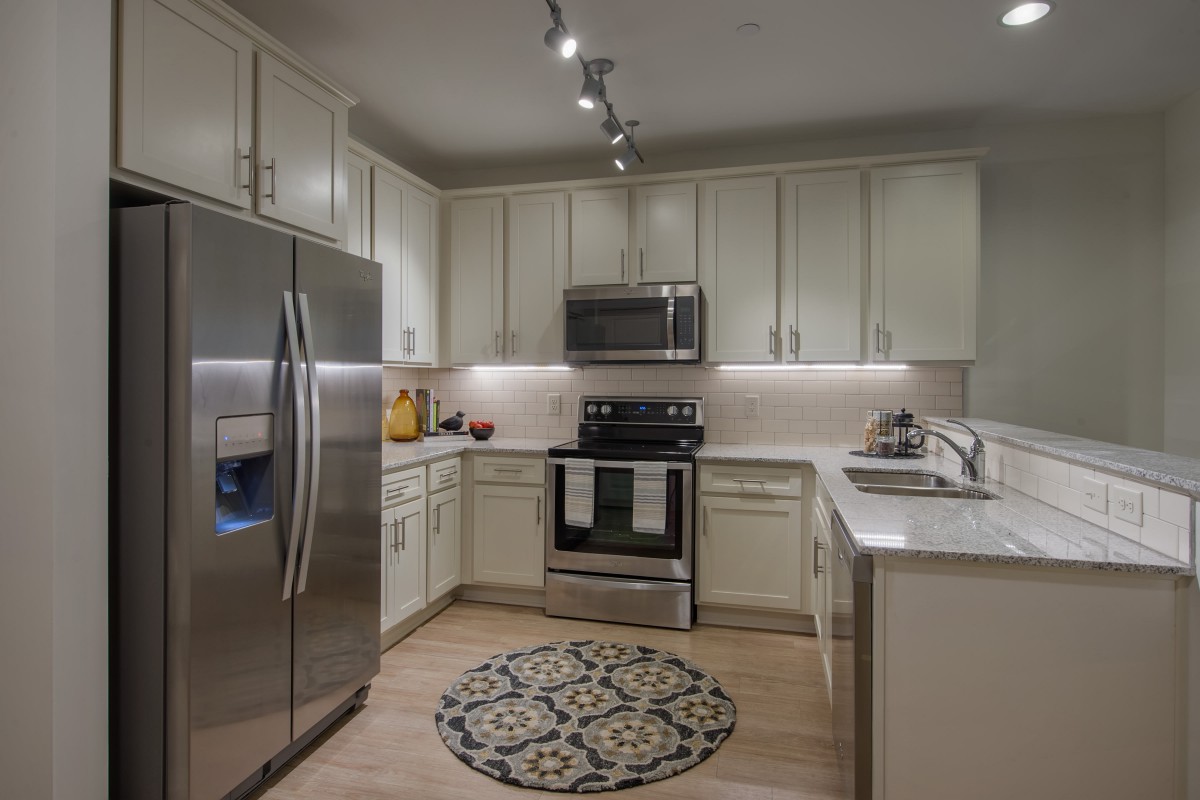 A modern kitchen featuring stainless steel appliances, white cabinets, and a decorative rug.