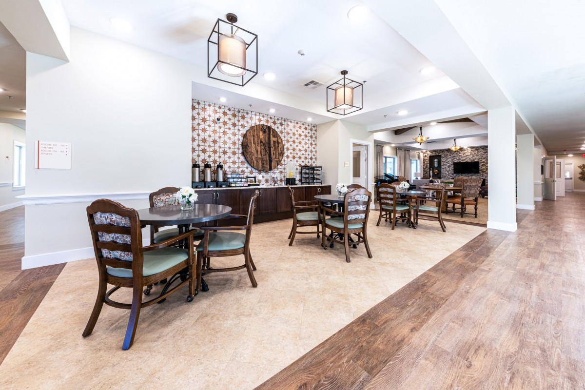 A spacious and elegantly designed dining area with wooden tables and chairs, featuring a coffee station and stylish lighting.