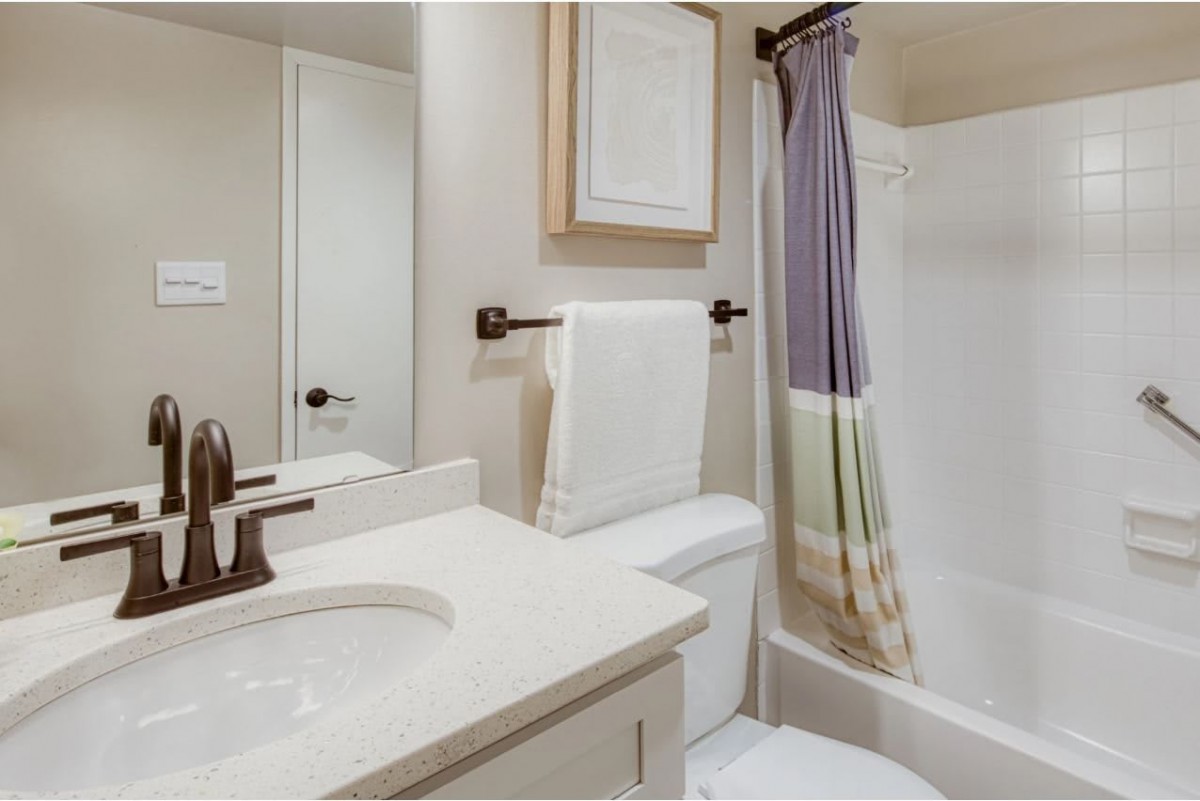 A clean and tidy bathroom featuring a sink with vanity, a towel rack, shower with curtain, and toilet.