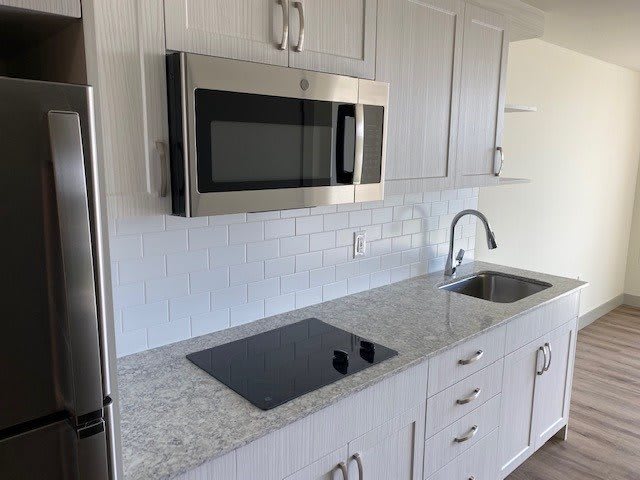 A modern kitchen setup with a microwave, stovetop, sink, and white cabinets.