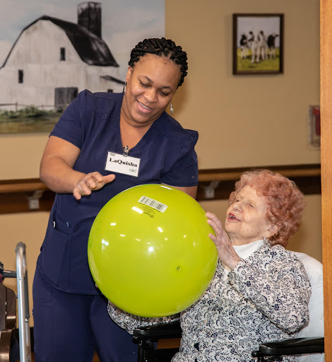 A caregiver engages with an elderly resident, bringing joy through playful interaction with a green ball.