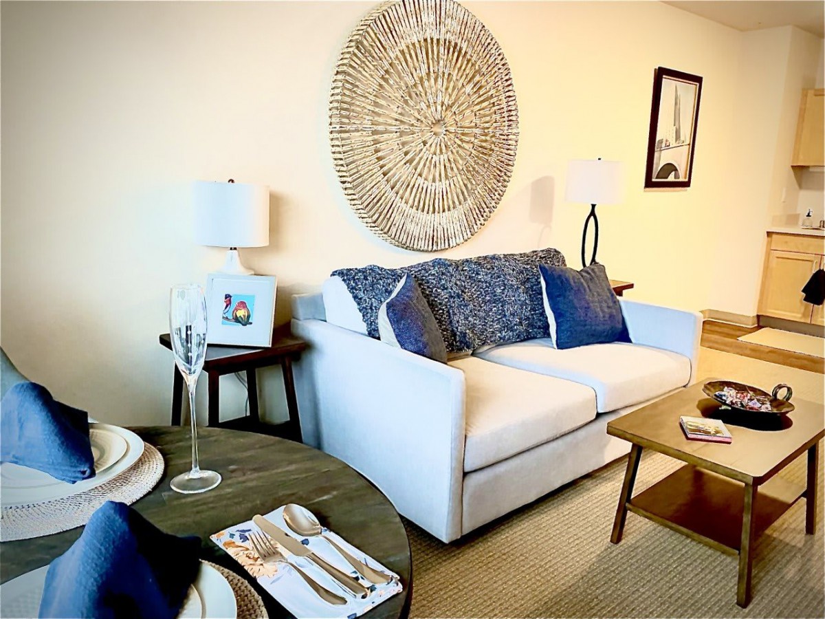 A cozy living room with a white sofa accented by blue pillows, featuring decorative wall art and modern furnishings.