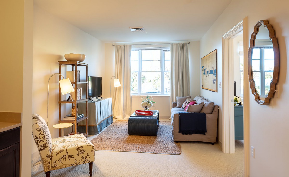 A cozy living room with a sofa, coffee table, and TV, complemented by a window letting in natural light.