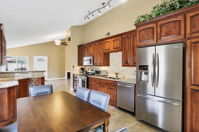 A modern kitchen with wood cabinetry and stainless steel appliances, featuring a dining area with a wooden table and chairs.