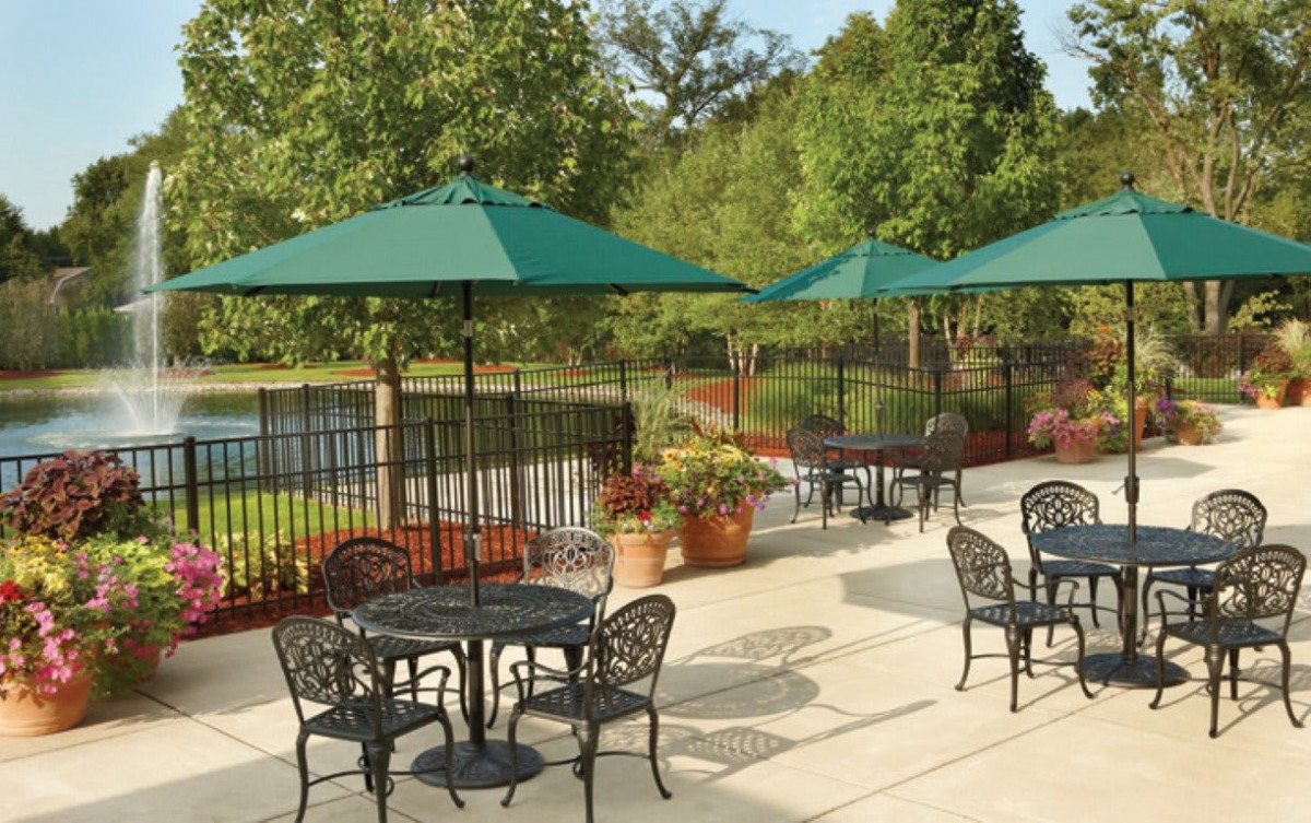 A scenic outdoor patio area with tables, chairs, and green umbrellas overlooking a pond.