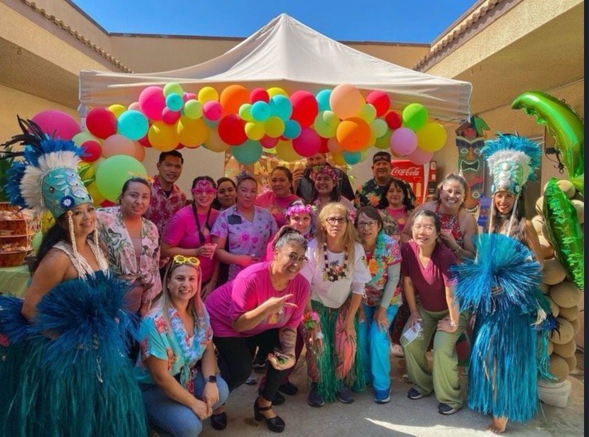 A lively group celebrates outdoors with colorful balloons and festive costumes.