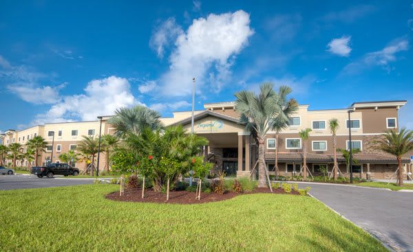 A modern hotel building surrounded by lush greenery and palm trees under a bright blue sky.