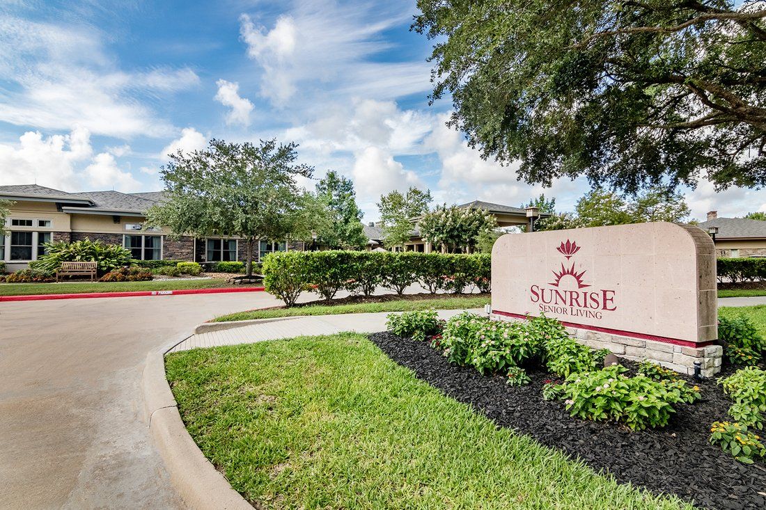 A scenic view of a building with well-maintained landscaping and a prominent entrance sign on a sunny day.
