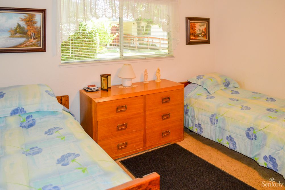 A cozy bedroom with twin beds, a wooden dresser, and a window overlooking the garden.