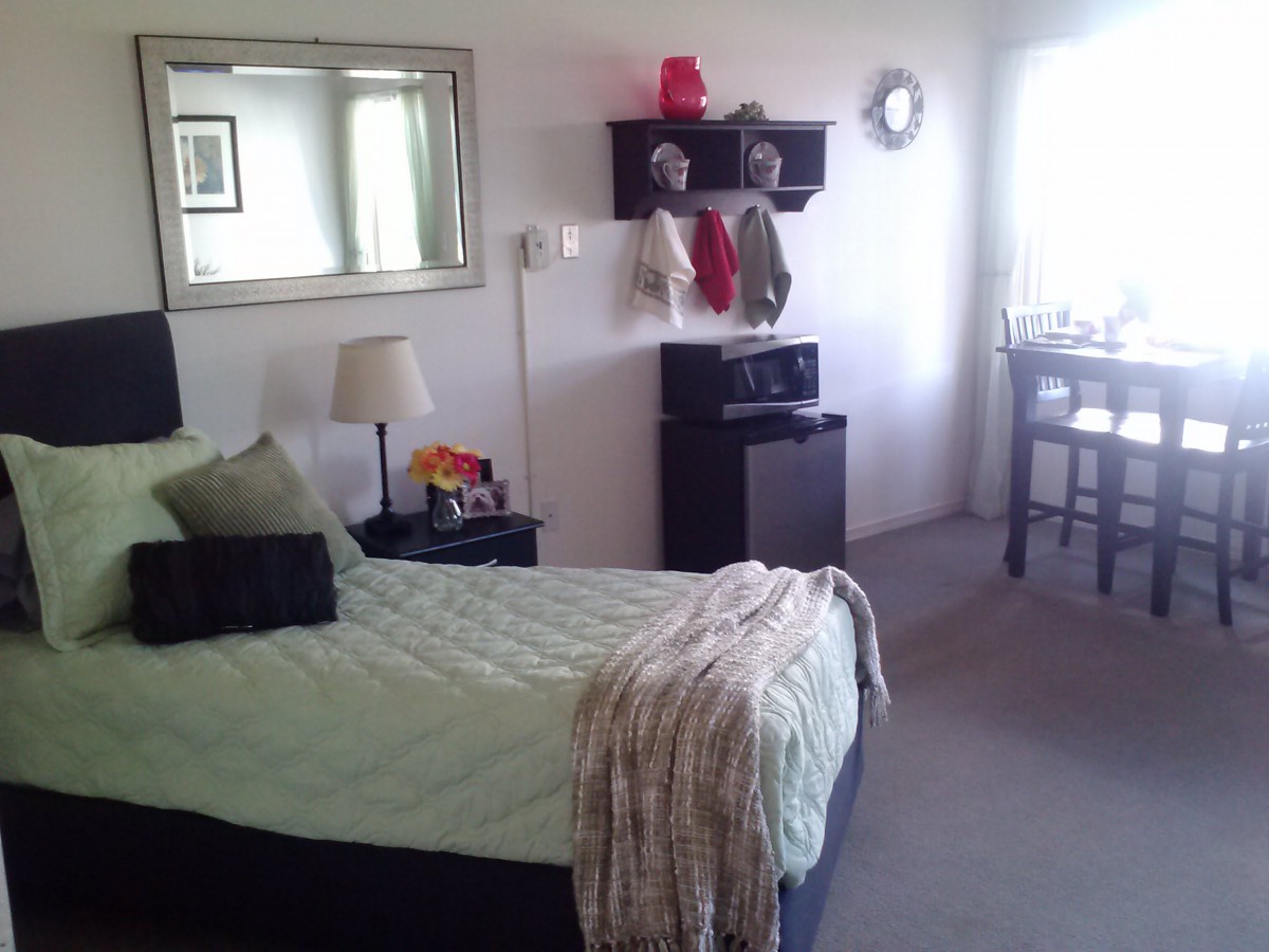 A cozy bedroom with a neatly made bed, wall mirror, and shelves adorned with hats and scarves.