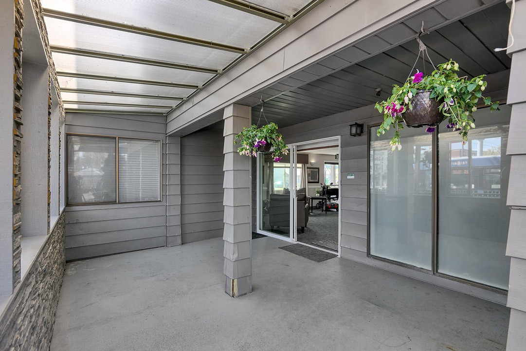 A covered patio with hanging plants and sliding glass doors leading inside.