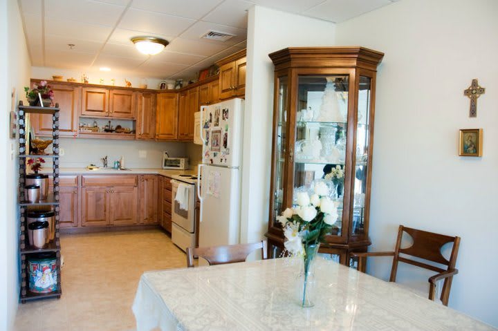 A cozy kitchen and dining area with wooden cabinets and a china cabinet, featuring a table adorned with a vase of flowers.