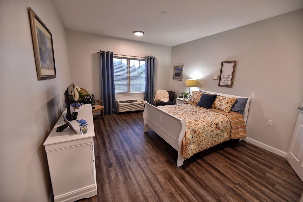 A cozy and well-decorated bedroom with a bed, bedside lamp, and large window.