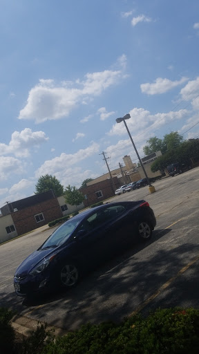 A parked blue car in an empty parking lot under a partly cloudy sky.
