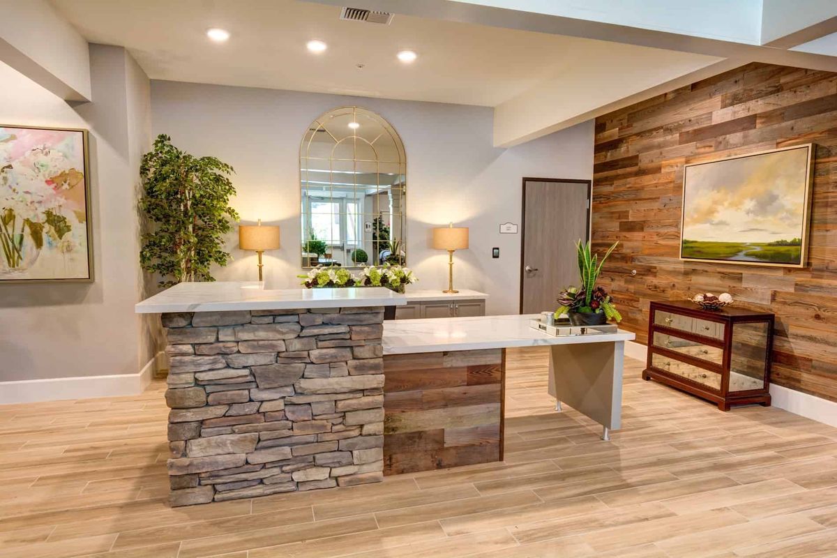 A modern reception area featuring a stone counter and wood flooring, accented with plants and warm lighting.