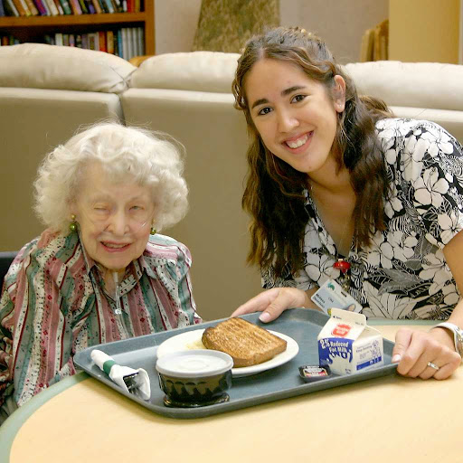 A joyful moment shared between a young volunteer and an elderly woman during meal time.