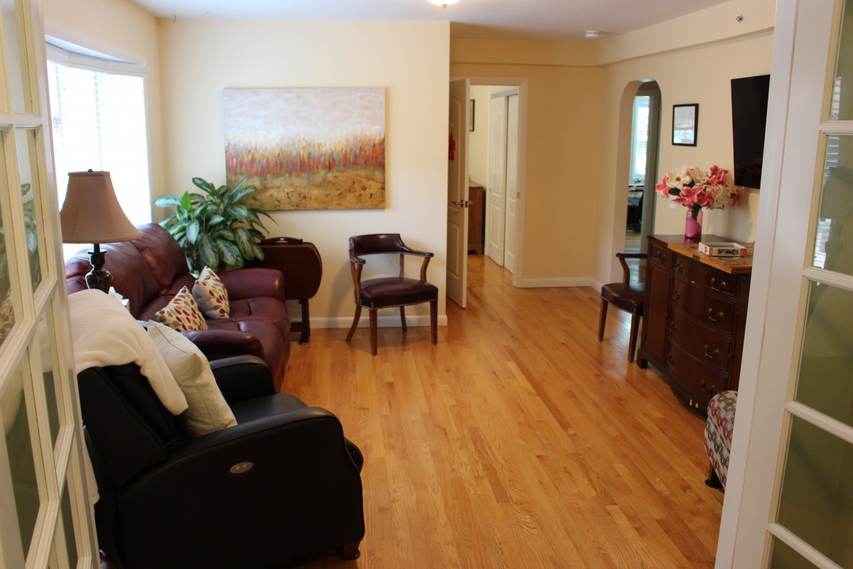 A cozy living room with a wooden floor, adorned with comfortable sofas, chairs, and a decorative painting.