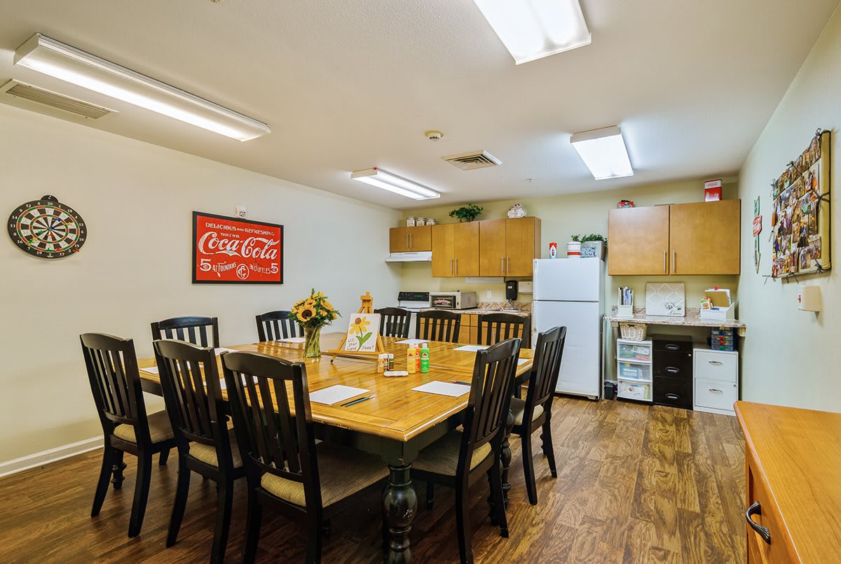 A cozy dining area with a kitchen setup, featuring a large wooden table surrounded by chairs, and equipped with modern appliances and decor.