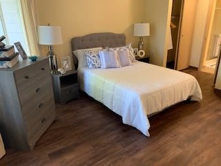 A cozy bedroom featuring a neatly made bed with decorative pillows, flanked by nightstands and lamps, and a dresser against the wall.