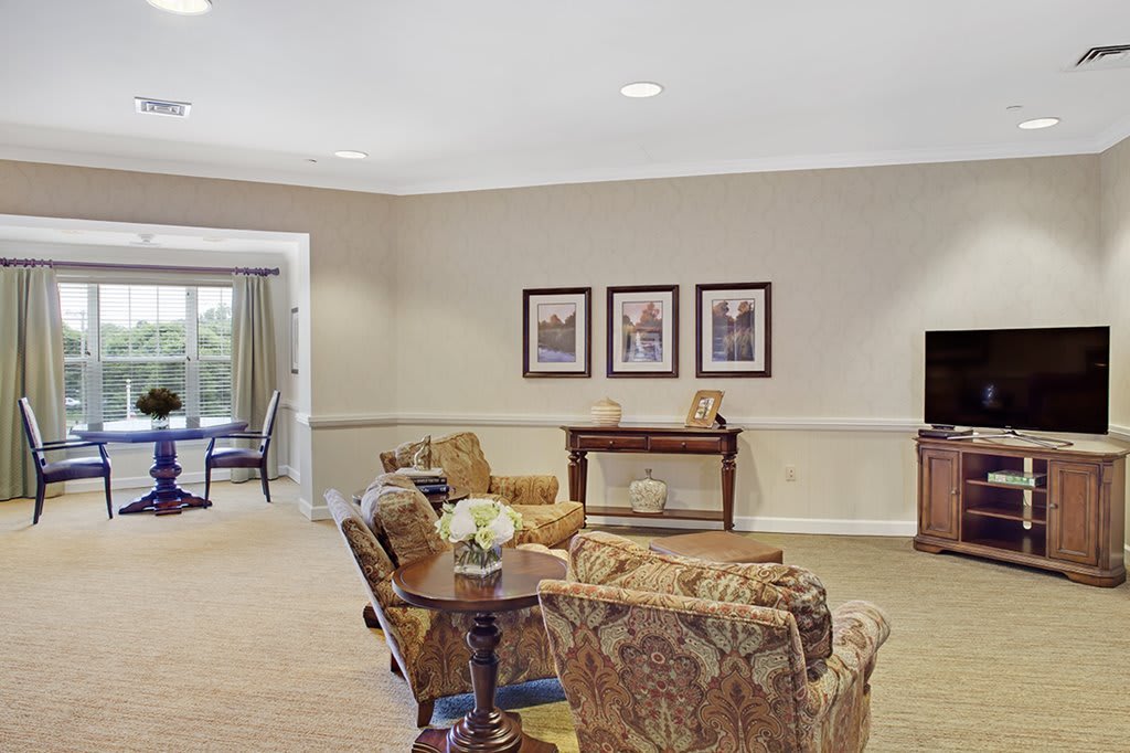 A cozy living room with floral patterned furniture, a TV, and framed art on the walls.