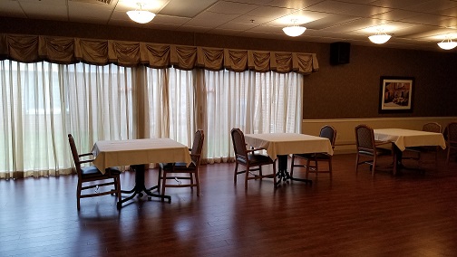 An interior view of a room with tables and chairs, featuring large windows draped with curtains.
