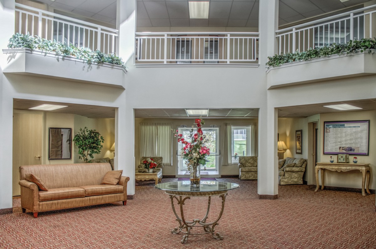 A spacious lobby with a central table displaying flowers, surrounded by comfortable seating and decorated with plants.