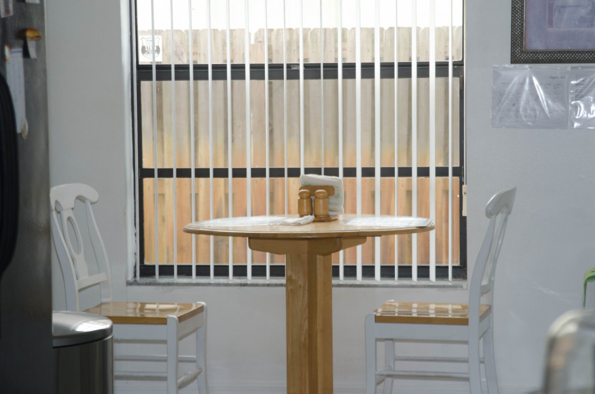 A simple dining setup with a wooden table and two chairs in front of a window with vertical blinds.
