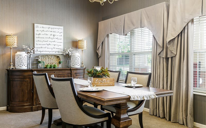 A stylish dining room with an elegant table and chairs, featuring a large window with drapes.