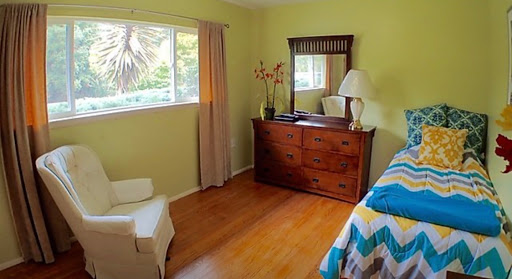 A cozy bedroom featuring a wooden dresser, mirror, and natural light coming through the window.