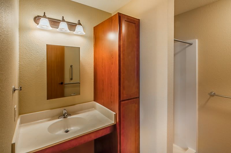 A modern bathroom featuring a sink with a mirror, wooden cabinet, and overhead lighting.