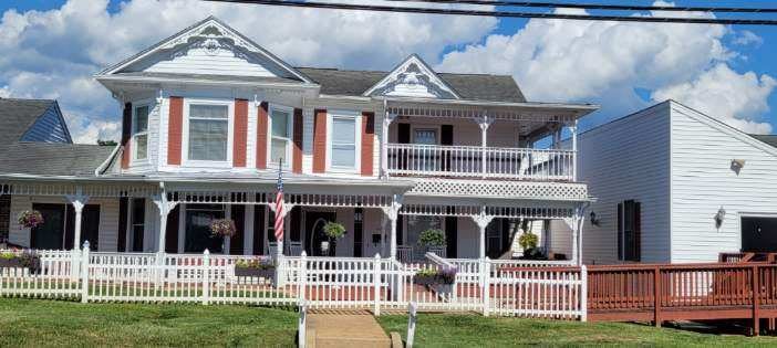 A charming Victorian-style house with a wide porch and white picket fence, set against a partly cloudy sky.