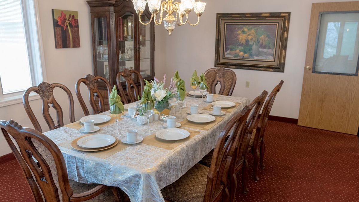 A formal dining room featuring an elegantly set table with dinnerware and a flower arrangement under a chandelier.