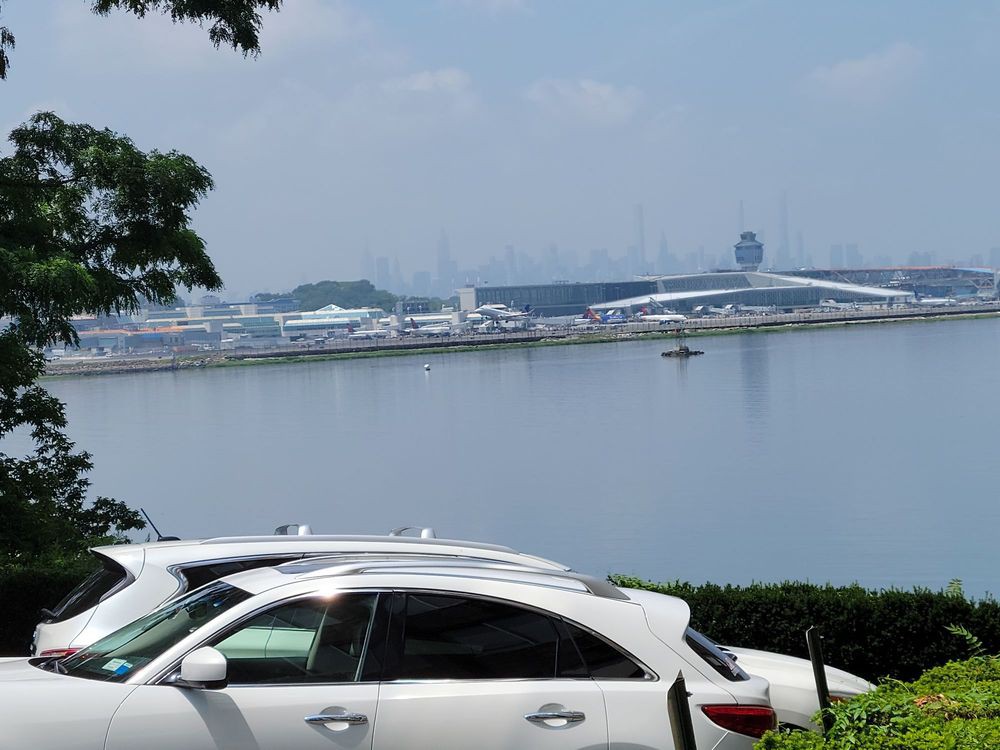 A scenic view of cars parked near a waterfront with modern architecture in the background.