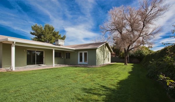 A spacious backyard with a single-story house and well-maintained lawn under a clear blue sky.