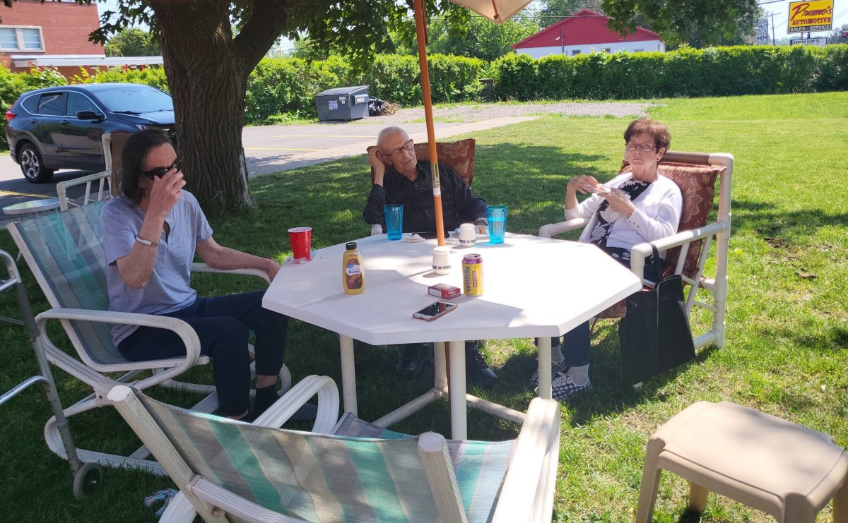 A group of people enjoying a sunny day sitting around an outdoor table under an umbrella.