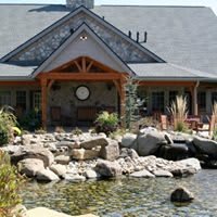A picturesque house with a wooden porch, surrounded by a landscaped garden and rocky pond.