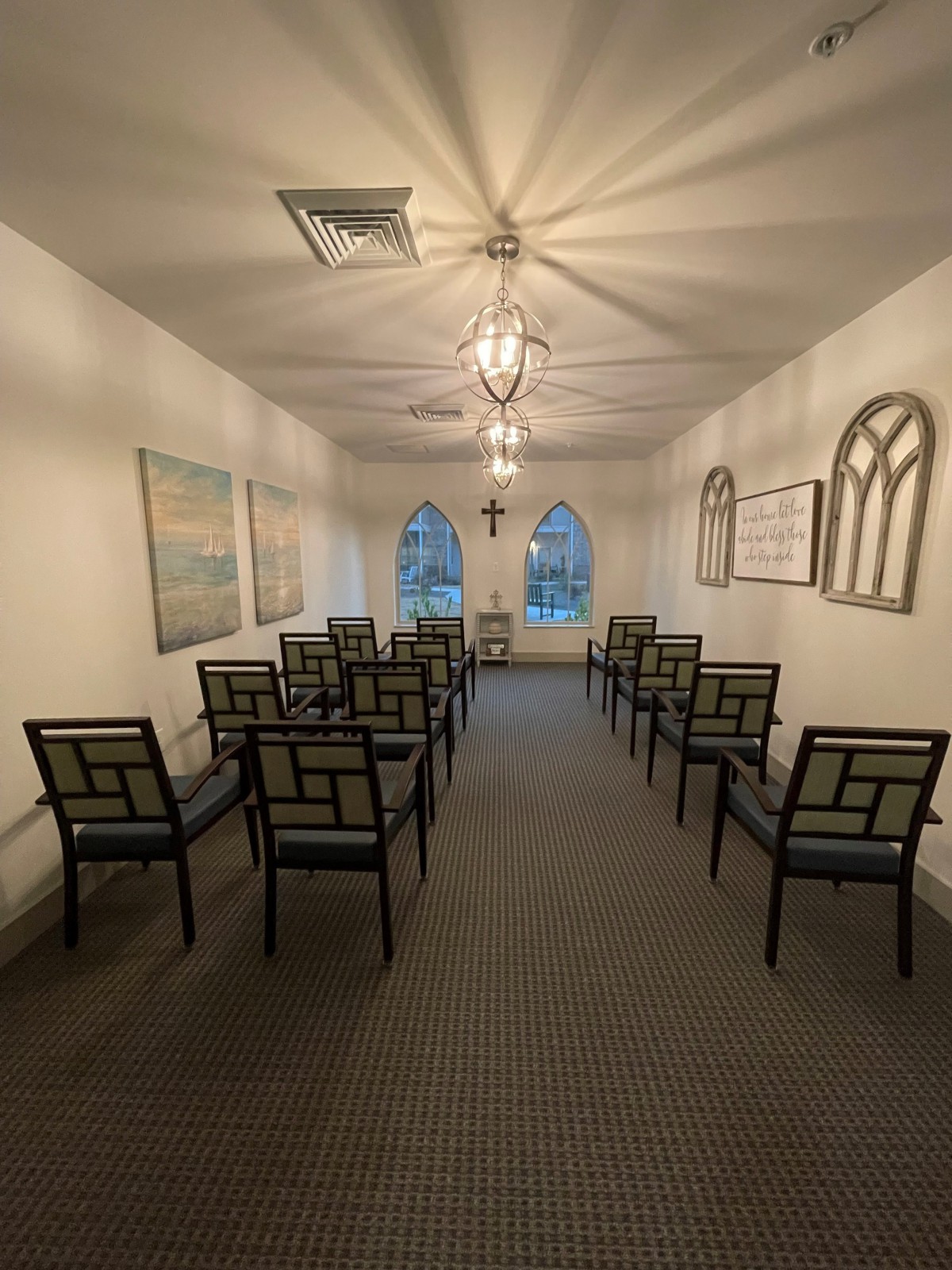 A small, symmetrical chapel with rows of chairs and a cross at the front, illuminated by soft lighting.