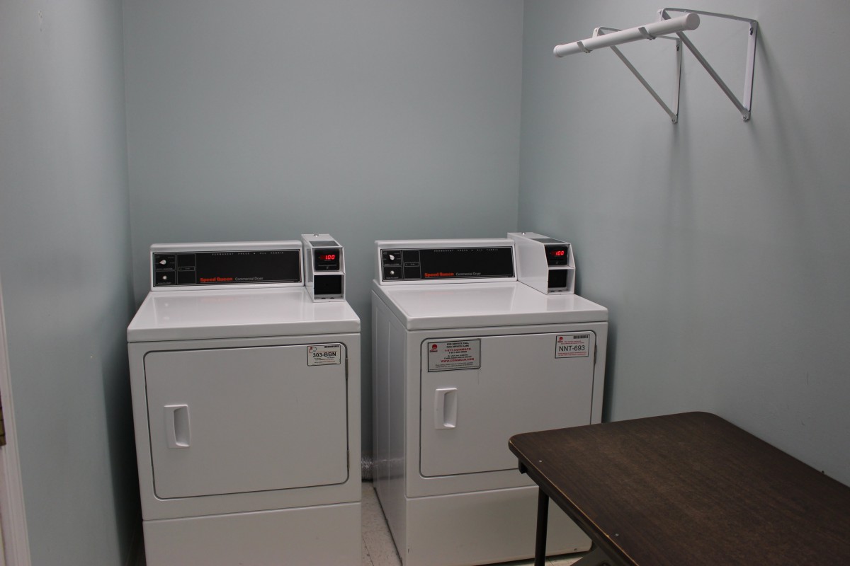 A laundry room featuring two dryer machines, a table, and a clothes rack.