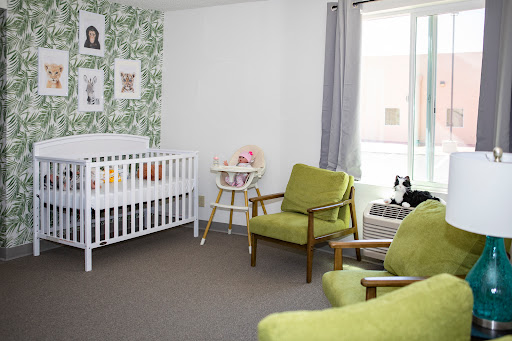 A cozy and stylish nursery featuring a white crib, green chairs, and lovely wall decor.