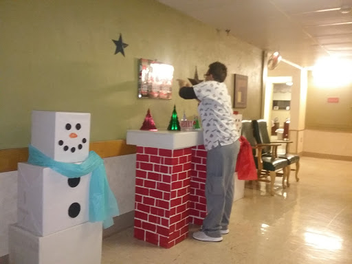 A person adding festive decorations to a holiday-themed display in a community space.
