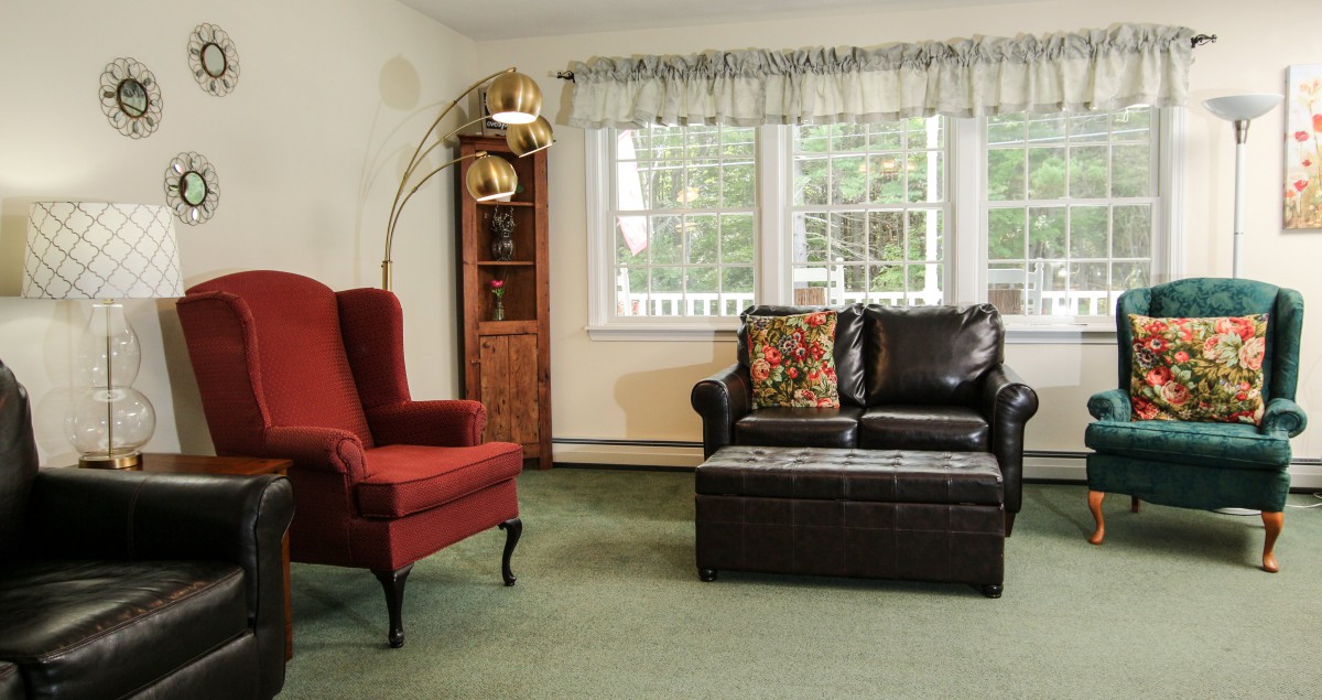 A cozy living room with a red armchair, a leather sofa, and a standing lamp by the window.
