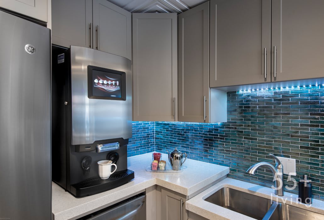 A modern kitchen corner featuring a coffee machine on the countertop next to a sink and stylish backsplash.