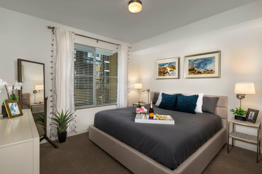 A modern bedroom with a stylish bed and elegant decor featuring artwork and a window view.