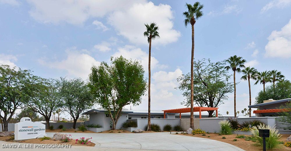 A mid-century modern house with tall palm trees set against a partly cloudy sky in a desert landscape.