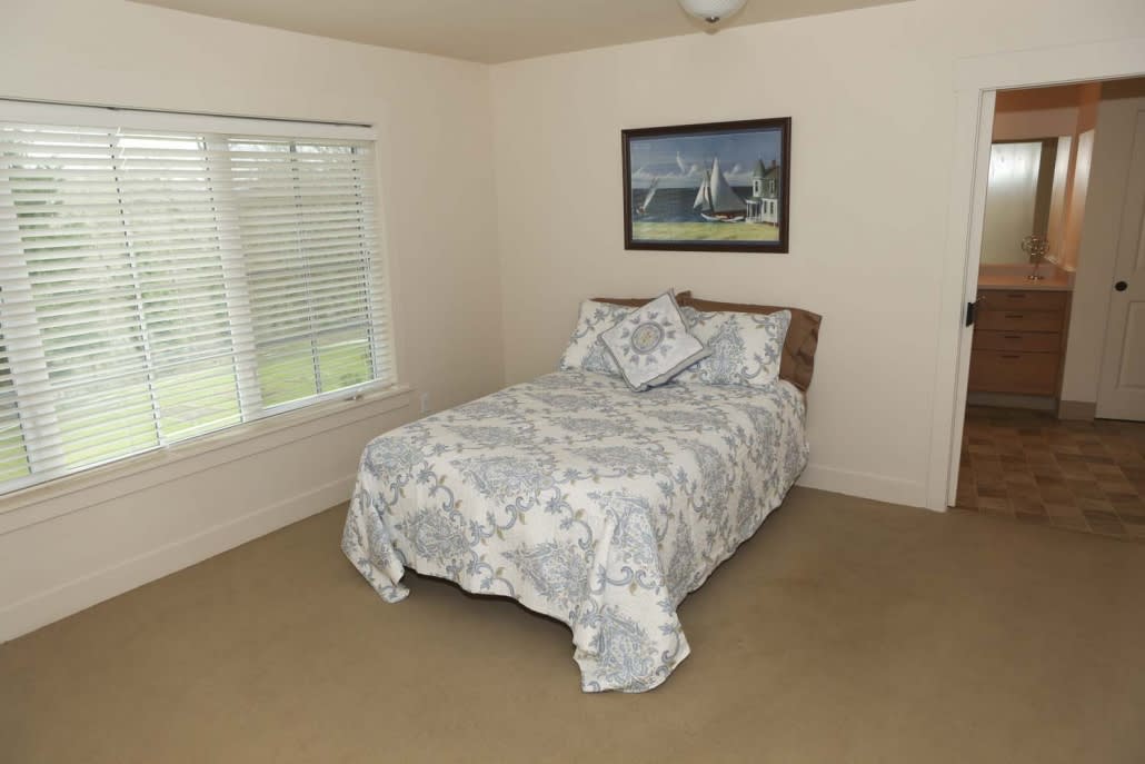 A neatly arranged bedroom with a bed, decorative bedding, and a painting on the wall.